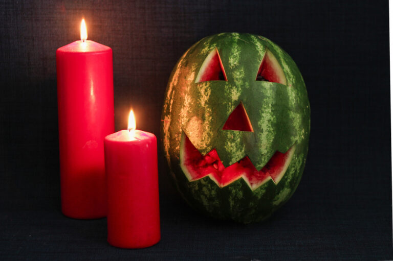 carved watermelon face with red candles and black background